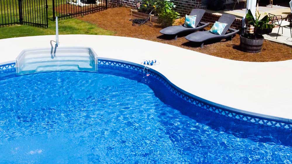 A beautiful blue kidney-shaped pool shimmers in the sunlight of a well-maintained backyard.